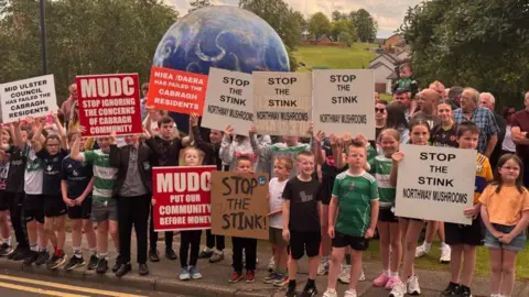 A large group of mainly children holding placards saying stop the stink. They are standing in front of an inflatable globe. 