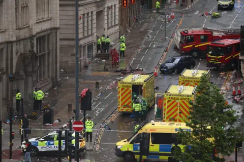 An aerial view of a street cordoned off by police, with ambulances, fire engines and uniformed police officers present.