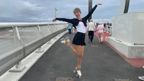Laura Foster/BBC Ellen Siegert posing on the Gull Wing bridge with her arms in the air and one leg raised