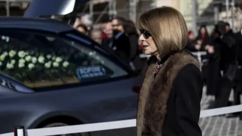 MASSIMO PERCOSSI/EPA/Shutterstock Anna Wintour wearing sunglasses and a fur-trimmed coat walks past a hearse near the funeral entrance