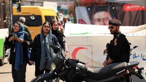 Reuters Iranian women walk past a police officer standing guard on a street, amid a ceasefire between the U.S. and Iran, at Tajrish Square in Tehran