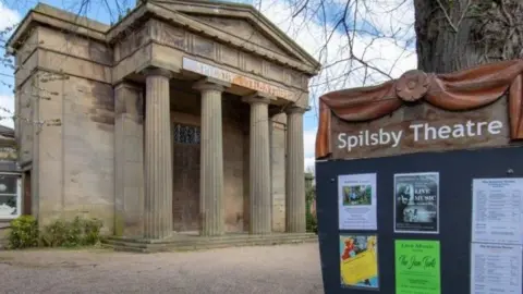 Spilsby Sessions House The exterior of Spilsby Sessions House. It is a historical building with four large columns at the front. A sign in the foreground reads "Spilsby Theatre" and has some posters on it with details of events. 