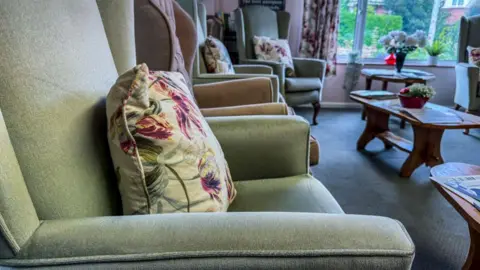 Getty The interior of a empty care home living room with four upright chairs with cushions on and three wooden tables.