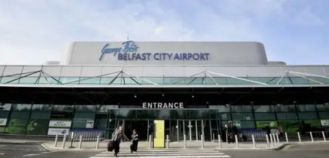 bbc Front entrance of George Best Belfast City Airport showing two people with hand luggage walking out