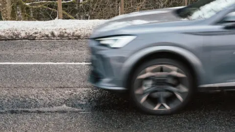 A car driving across the road with snow at the sides of the road