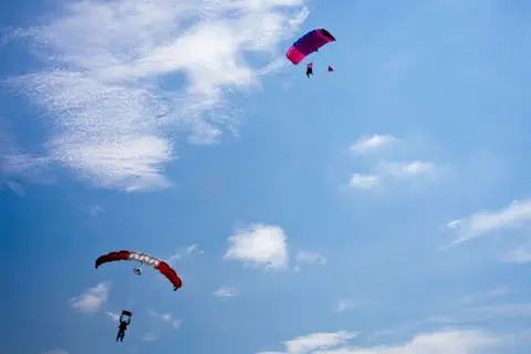 The Boston Globe via Getty Images Two tandem skydivers open their parachutes after free falling