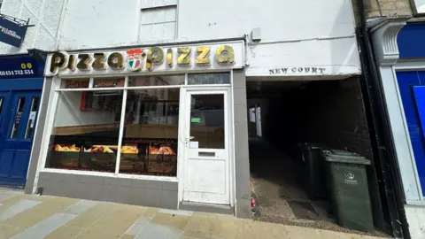 A pizza store  with an alleyway beside it.