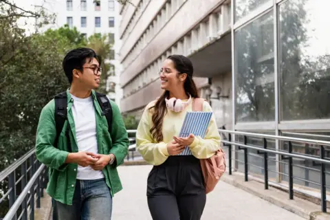 EF Volart/Getty Images A man and a woman, both in glasses, smile and talk as the walk past a large university building