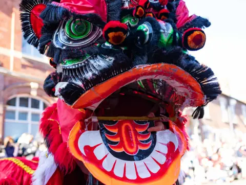 Museum of Royal Worcester A costume with several colours. Crowds in sunlight and buildings are blurred in the background.