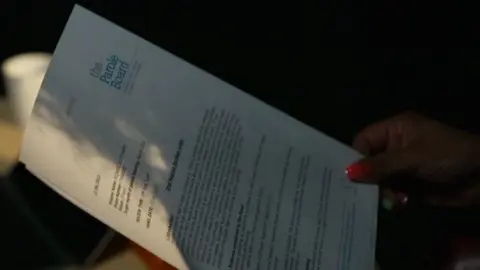 A hand is seen holding a sheet of A4 paper that has typed writing on it in black