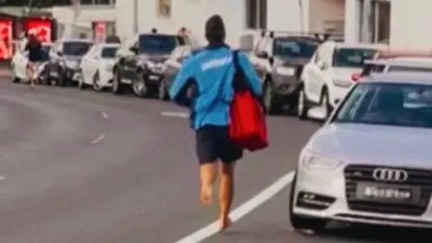 A lifeguard runs down a road barefoot