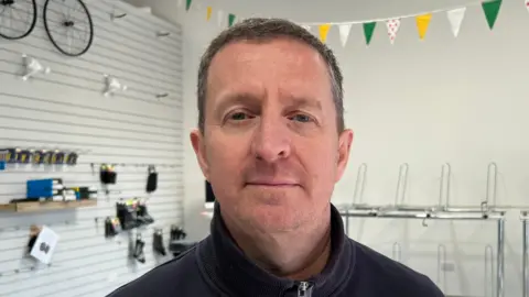 Mark Reynolds standing in his shop with empty shelves behind him