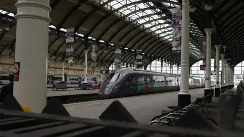 A train at one of the platforms inside the station. The station has a large arched glass roof with white pillars running along the length of the platform.