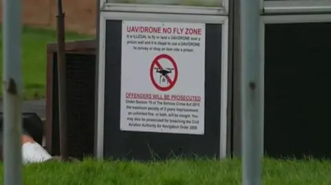 A small road sign outside HMP Long Lartin warns that the prison now has a "UAV/Drone No Fly Zone". The sign states it is illegal to fly or land over a prison wall, and stresses offenders will be prosecuted