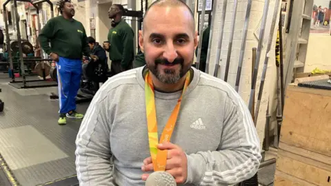 Ali Jawad, who holds his silver Paralympic medal around his neck, smiles as he poses for a photo at the club 