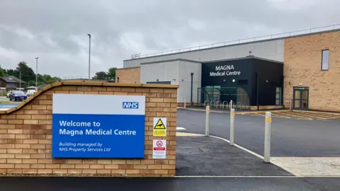 David Freezer/BBC Image shows entrance to a medical centre's car park, with the medical centre visible in the background on a grey, cloudy day.