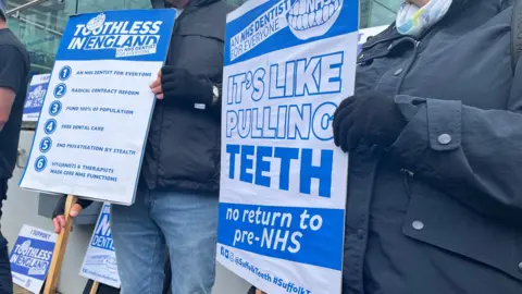 Connor Bennett/BBC A close-up of one of the campaigner's holding a poster. It reads: "It's like pulling teeth, no return to pre-NHS"