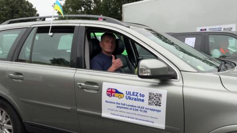 Man sitting in a car with a Ukraine flag giving a thumbs up