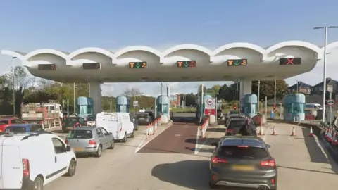 Google Street View image of cars queueing up to use white and blue-coloured toll booths at the Tamar Bridge.