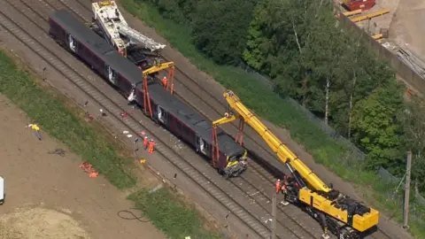 The end of a train carriage which has been damaged is attached to a crane