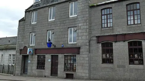 Geograph/Stephen Craven The Blue Lamp. The venue has a blue map above a brown door and panelling. It has a McEwan's Ale sign. 