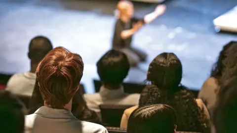 Getty Images An audience look on at a performer kneeling on a stage