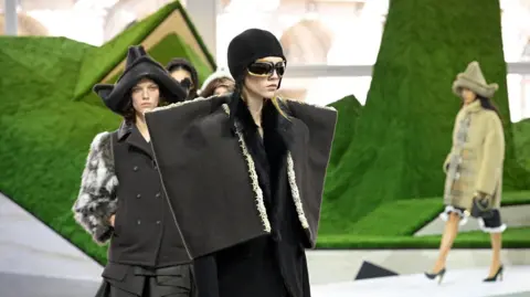 Getty Images Models wearing wide-shouldered jackets and conical hats at Louis Vuitton show