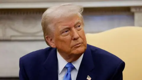 Trump in blue suit sitting in yellow chair looking to side