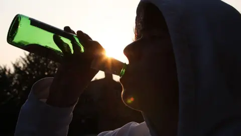 Generic image of a teenage boy in shadow drinking a bottle of lager