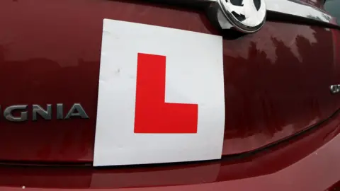 PA Media A picture of the back of a red car with an L plate on it. It is a red car with silver writing on it.