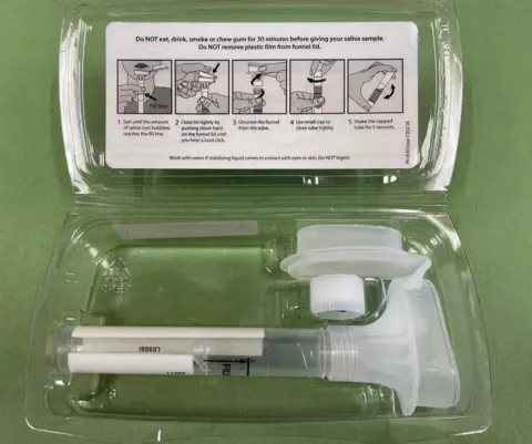 Institute of Cancer Research/PA Wire Photo shows the aliva test kit, in a plastic tray is what looks like a large plastic syringe tube and other parts, with instructions for how to use it, sitting on a green table.