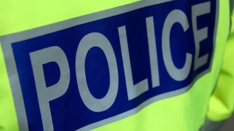 The back of a police officer's jacket showing the word "police" in silver letters on a blue background.