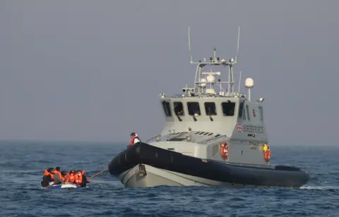 A Border Force boat interacting with a small boat filed with suspected migrants