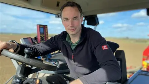 Farmer James Price on a tractor. He is looking at the camera.