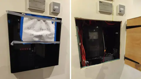 RICHARD SPENCER Two images of the same fire alarm system, a black box on a cream wall. The left images shows the front panel closed, covered by a hand-written sign that reads "NOT IN USE: SEE PANEL ON 1ST FLOOR." The right image shows the front panel open with a few wires inside a dark area.