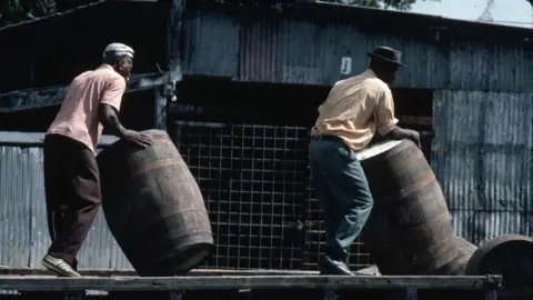 Getty Images/Tony Arruza Two men rolling rum barrels 