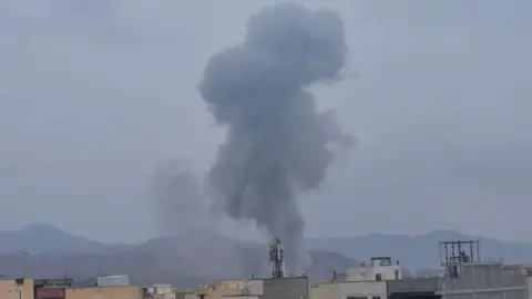 Supplied Grey smoke rises into the sky during the day on 10 March over Tehran, buildings and mountains visible in the background.