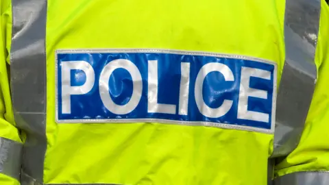 Getty Images The back of a police officer's yellow high-vis jacket. There is a blue band at the back with "POLICE" written on it in white text.