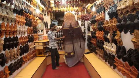 Getty Images A shopkeeper showcasing a life-size Kolhapuri sandal, surrounded by footwear on display in a shop.