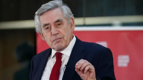 Grey-haired Gordon Brown wearing a dark suit, red tie and white shirt