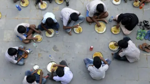 AFP via Getty Images Students eat their mid-day meal during lunch break at a government high school on the outskirts of Hyderabad on November 23, 2021