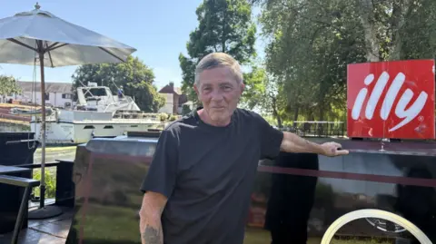 Mr Jefferys pictured wearing a black t-shirt stood next to a black narrowboat.