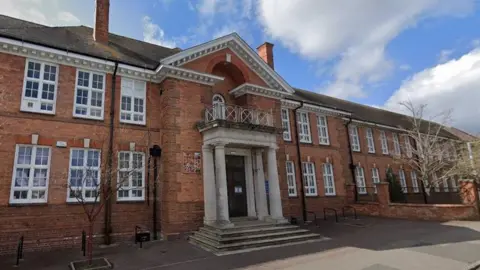 The exterior of the school, which is an older two-storey building with an impressive porch entrance and lots of windows. 
