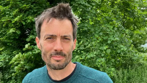 Guy Campbell/BBC The Greens candidate standing in front of a tree wearing a green jumper 
