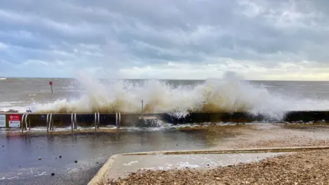Paul Smith Waves splash over a wall by the sea. Puddles are on the other side.