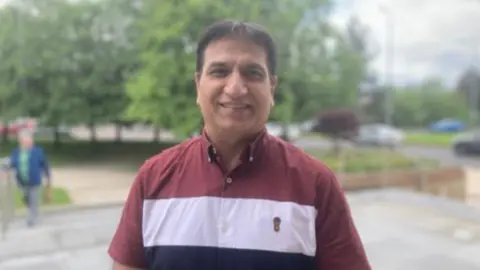 Dr Mukesh Chugh. He has dark hair, wearing a red, white and navy shirt.