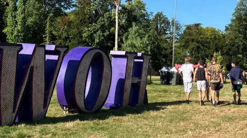 Festivalgoers walking past a large freestanding purple WOH sign