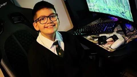 Family Twelve-year-old Azaan Khan in his school uniform sitting next to a computer 