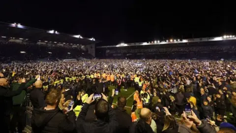 PA Media Crowds of fans on the Fratton Park pitch at night after a match