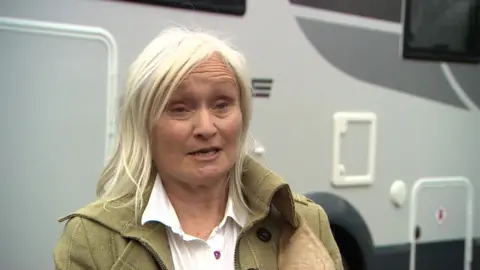 Joanne Fenton, with blonde, shoulder-length hair, stood outside a motorhome looking towards a camera